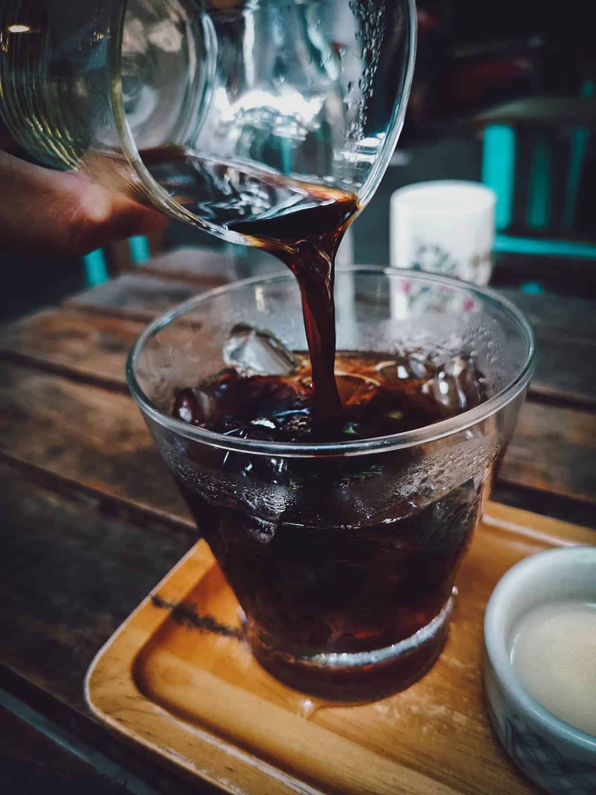 Pouring coffee into a glass with ice at Phin Coffee in Hoi An, Vietnam