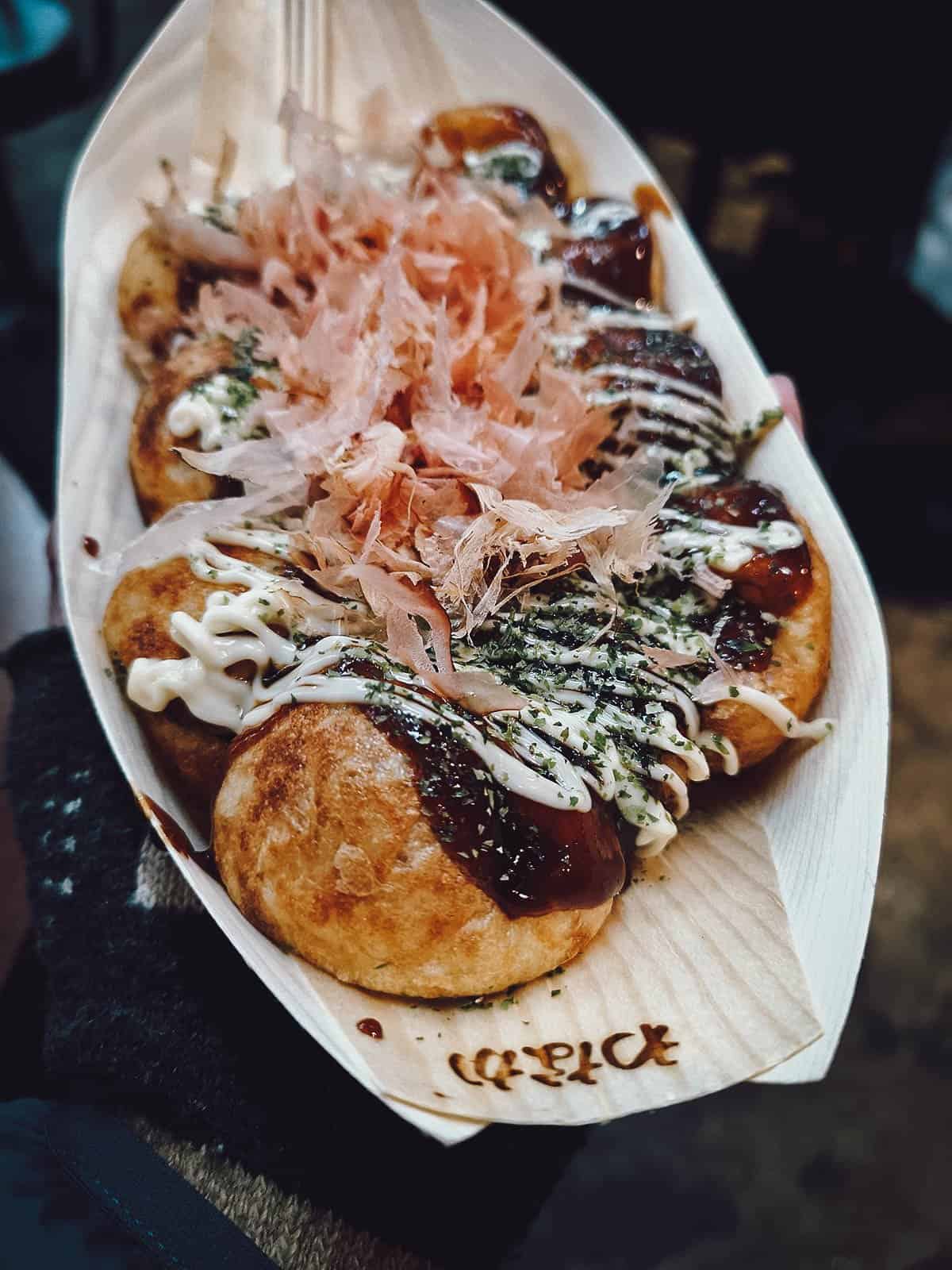 Takoyaki topped with bonito flakes, tempura scraps, and a brown sauce