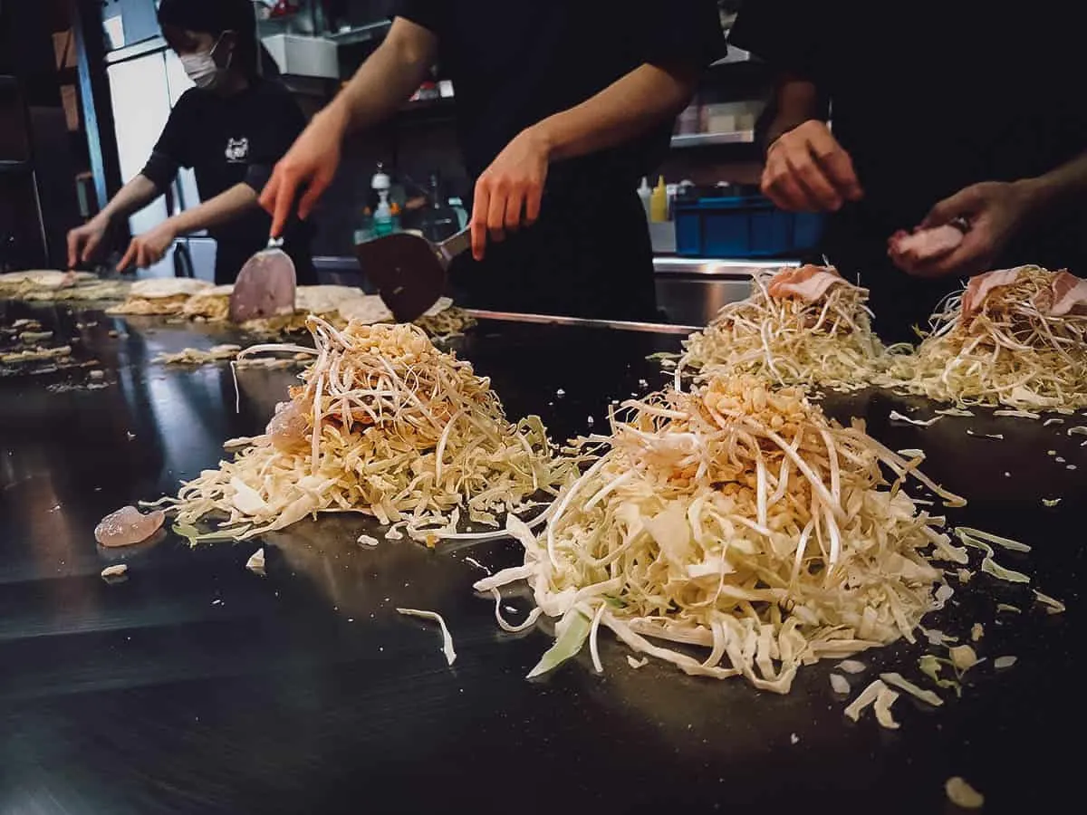 Cooks making okonomiyaki on a teppanyaki grill