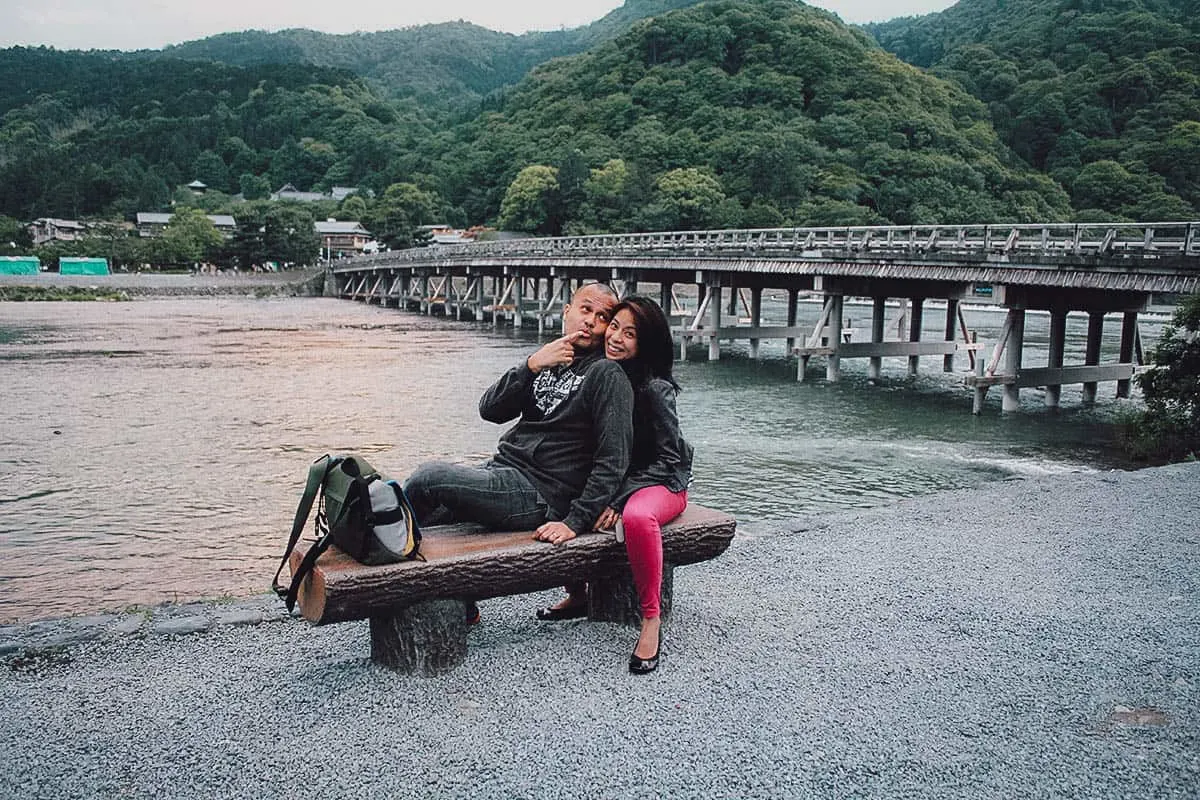Man and woman on a bench with Kyoto's Togetsukyo Bridge in the background
