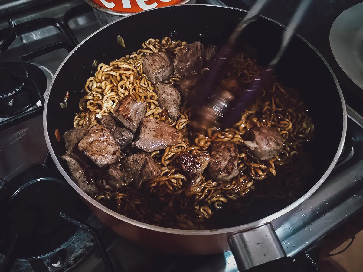 Adding the steak cubes to the noodles