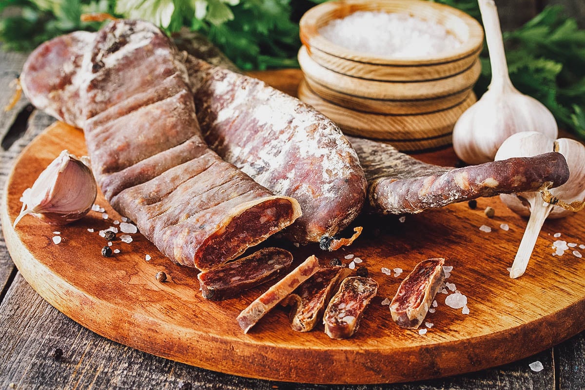 Sujuk on a chopping board with garlic and salt