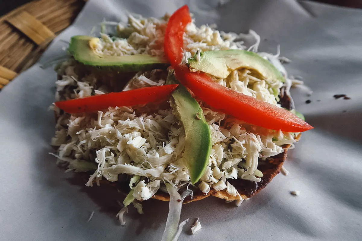 Tostada topped with Oaxacan string cheese, avocado, and tomato