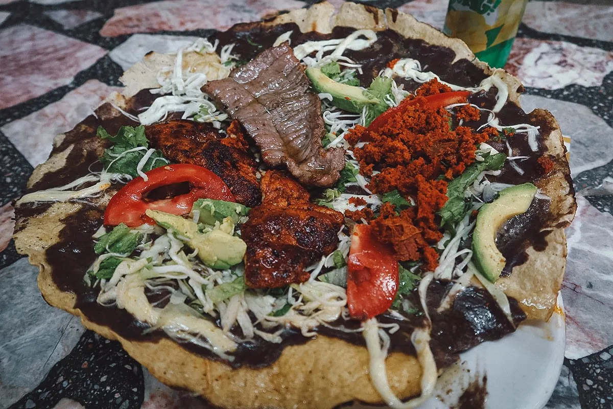 Oaxacan Food Tlayuda topped with pork lard, refried beans, Oaxacan string cheese, and roasted meat