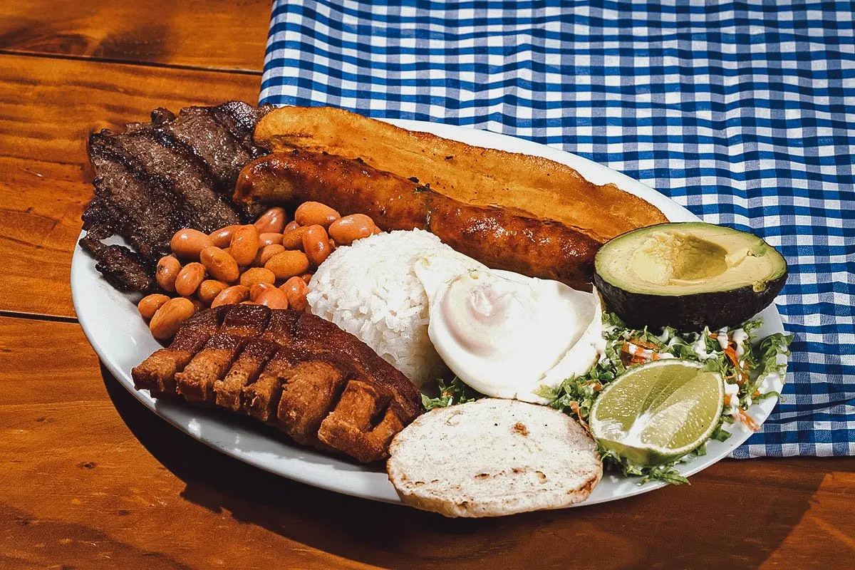 Bandeja paisa platter with different meats, beans, arepa, avocado, and a fried egg